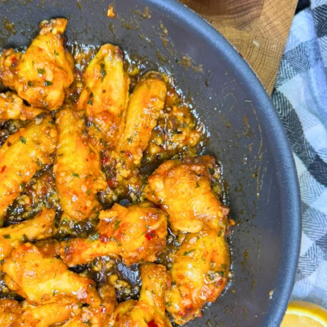 Sticky air fryer sweet chili chicken wings served on a plate with a fresh lemon wedge.