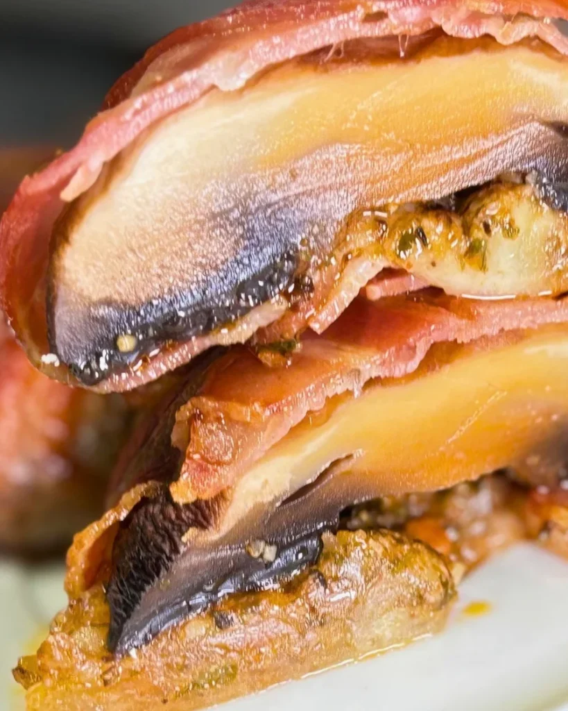 Detailed close-up of sliced bacon-wrapped mushrooms filled with melted mozzarella, garlic, thyme, and herbs.