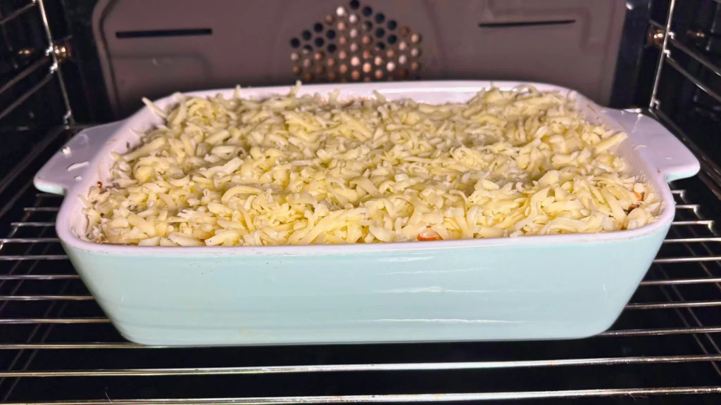 White ceramic baking dish filled with mashed potatoes, creamy chicken and mushroom filling, and shredded mozzarella placed inside the oven.