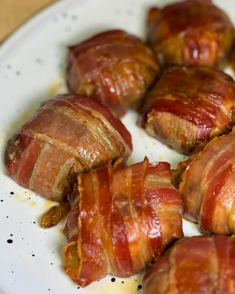 Golden bacon-wrapped mushrooms stuffed with melted mozzarella, served on a white plate.