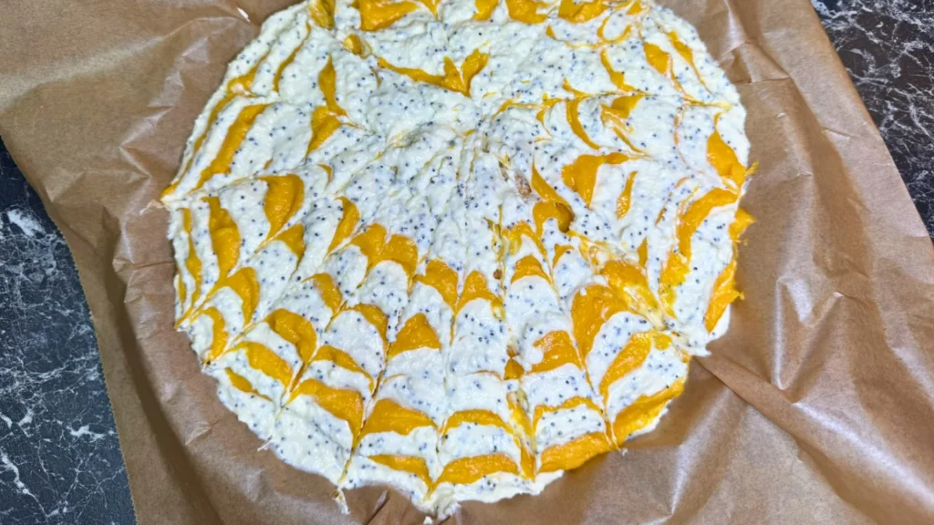Unbaked pumpkin and cottage cheese casserole with orange and white swirls, poppy seeds, and a decorative marble pattern on parchment paper.