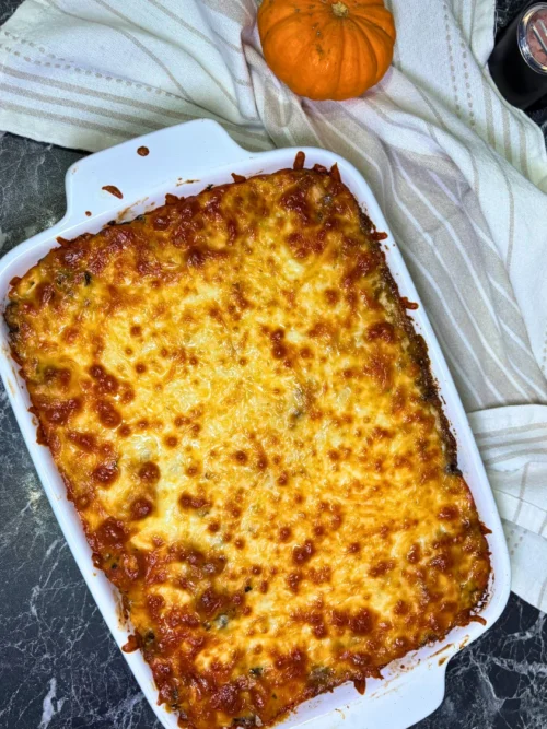 Overhead view of a freshly baked chicken and mushroom potato casserole with a golden-brown mozzarella topping in a white ceramic baking dish.
