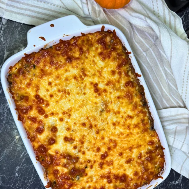 Overhead view of a freshly baked chicken and mushroom potato casserole with a golden-brown mozzarella topping in a white ceramic baking dish.
