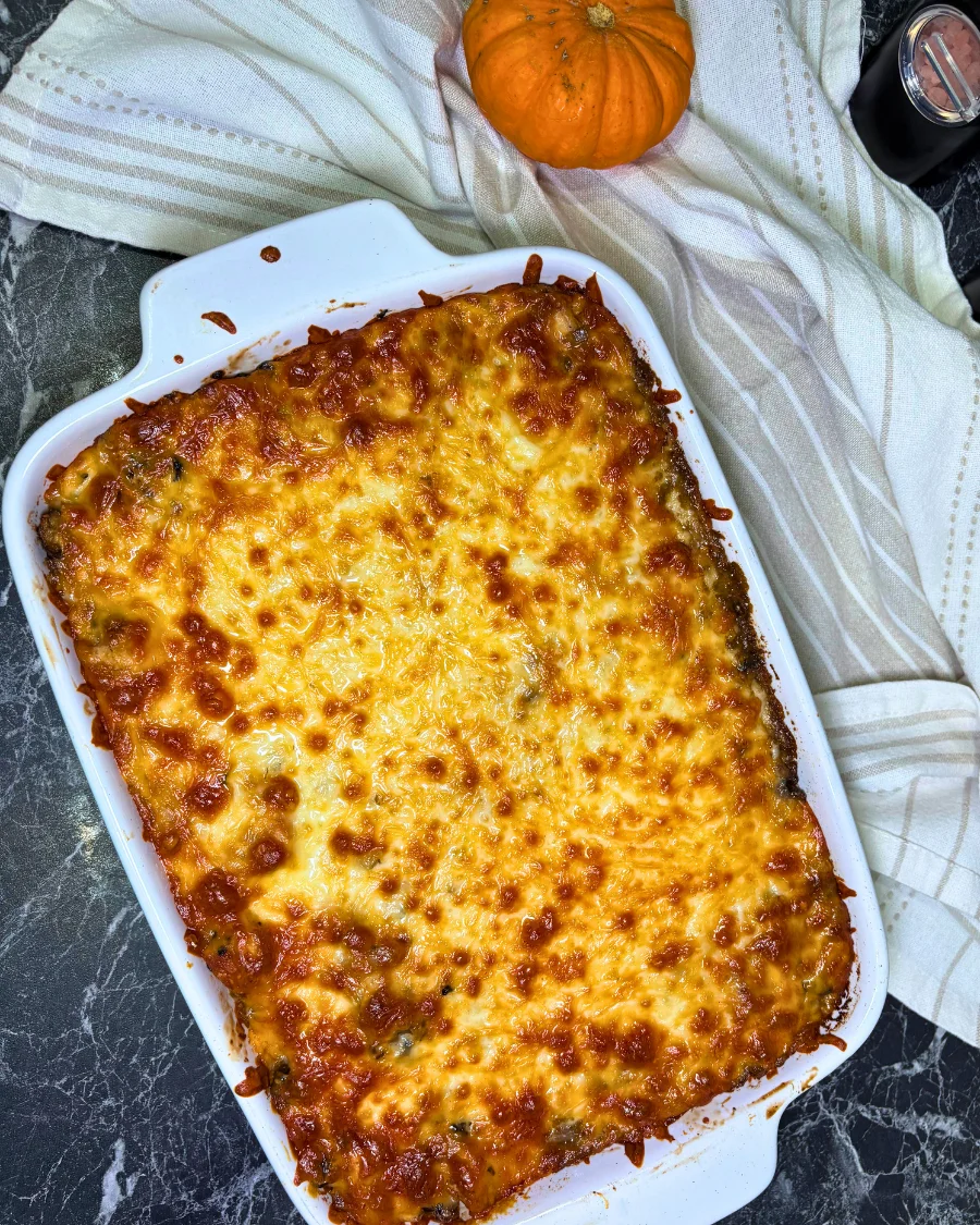 Overhead view of a freshly baked chicken and mushroom potato casserole with a golden-brown mozzarella topping in a white ceramic baking dish.