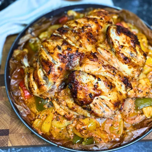Whole marinated chicken roasted until golden brown, surrounded by seasoned potatoes, bell peppers, onions, and garlic.