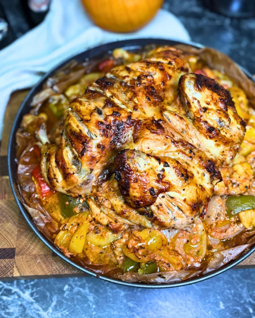 Whole marinated chicken roasted until golden brown, surrounded by seasoned potatoes, bell peppers, onions, and garlic.