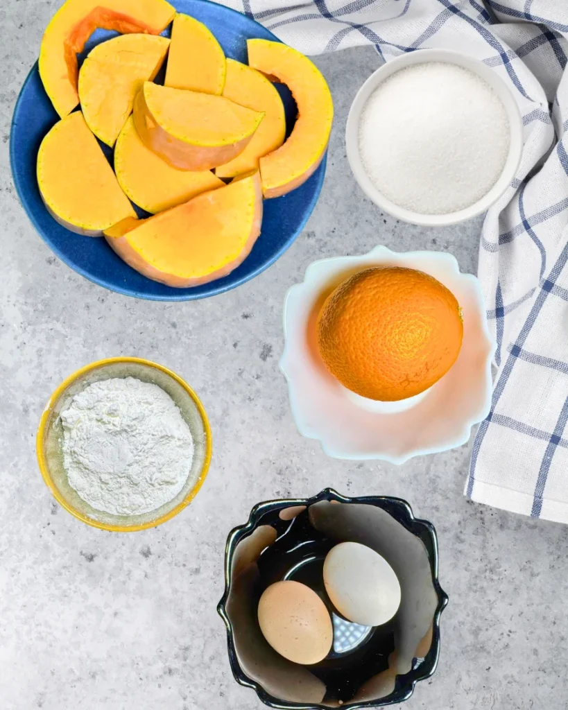 Fresh pumpkin slices, eggs, orange, sugar, and cornstarch arranged on a kitchen counter for homemade pumpkin casserole.
