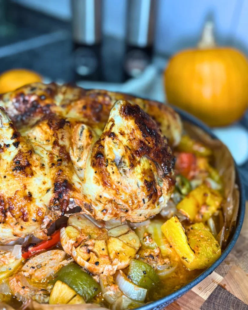 Golden oven-baked marinated whole chicken served with roasted potatoes, colorful bell peppers, onions, and garlic in a baking tray.