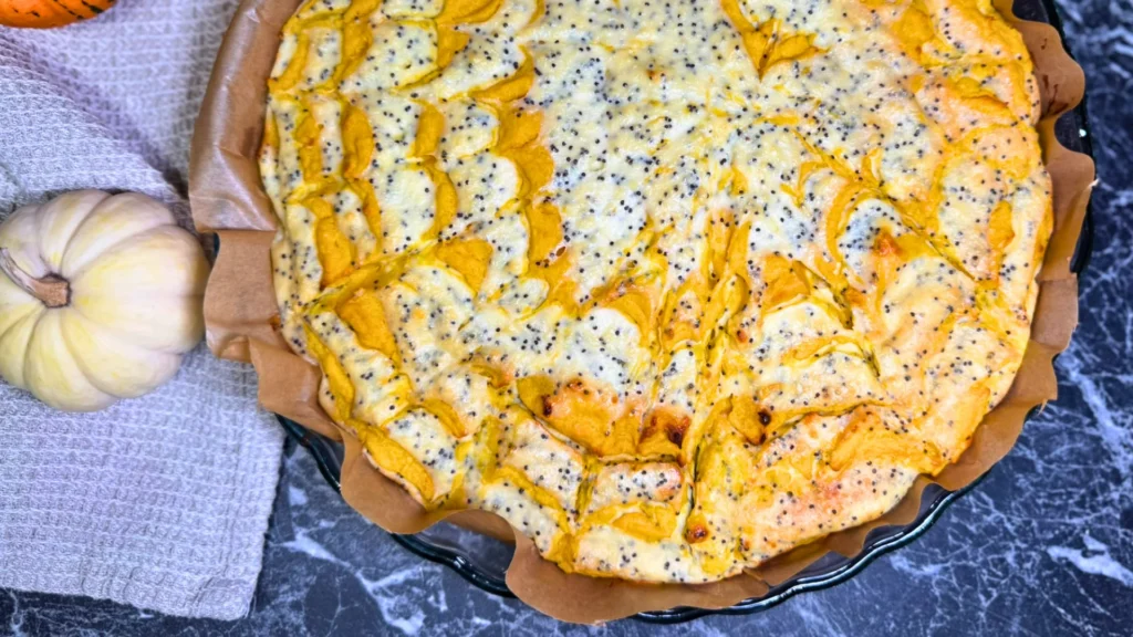 Freshly baked marble pumpkin and cottage cheese casserole in a parchment-lined baking dish, with orange pumpkin swirls and poppy seeds.