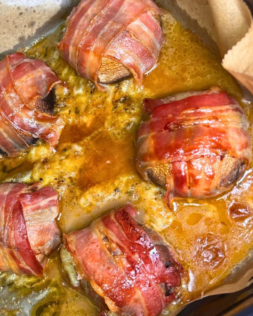 Freshly baked mushrooms wrapped in crispy bacon, surrounded by melted mozzarella, herbs, and flavorful cooking juices.