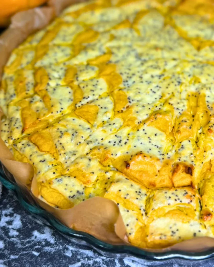 Overhead view of a baked pumpkin and cottage cheese casserole with a golden marble pattern and black poppy seeds, next to a small white pumpkin.