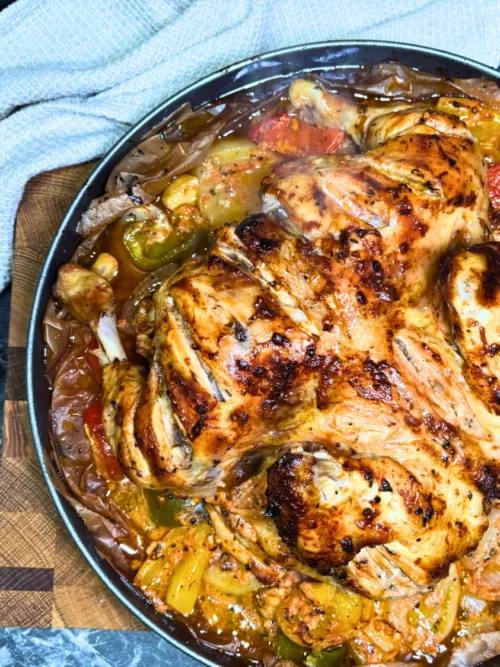 Detailed close-up of oven-baked chicken with browned skin, roasted potato slices, yellow and green bell peppers, and flavorful pan juices.