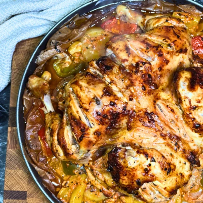 Detailed close-up of oven-baked chicken with browned skin, roasted potato slices, yellow and green bell peppers, and flavorful pan juices.