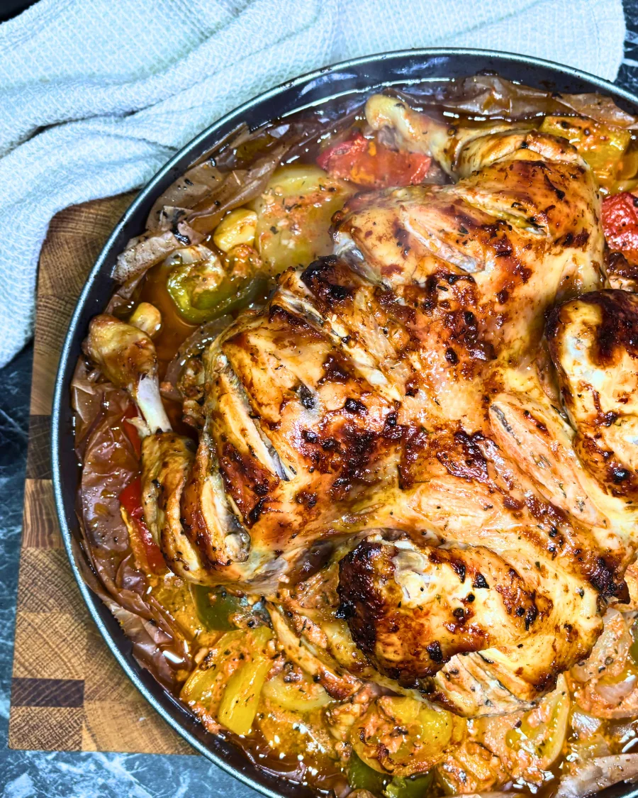 Detailed close-up of oven-baked chicken with browned skin, roasted potato slices, yellow and green bell peppers, and flavorful pan juices.