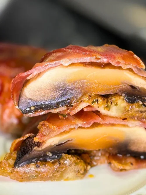 Close-up of bacon-wrapped mushrooms cut in half, showing juicy mushroom layers, melted mozzarella, and seasoned filling.
