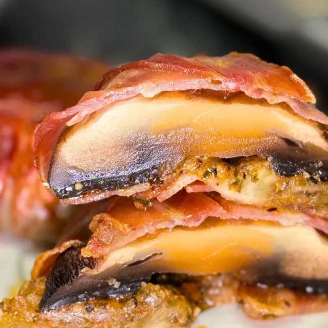 Close-up of bacon-wrapped mushrooms cut in half, showing juicy mushroom layers, melted mozzarella, and seasoned filling.