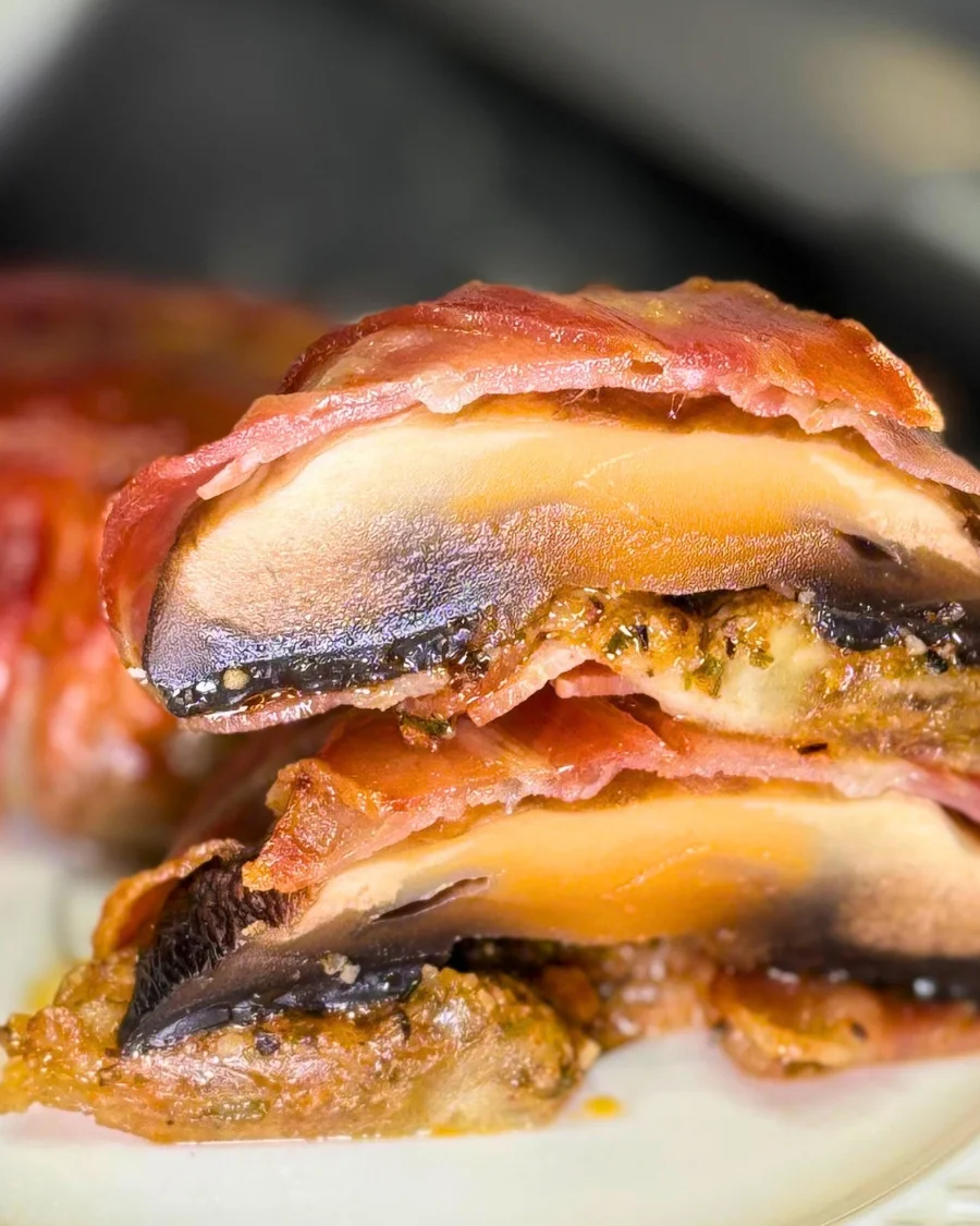 Close-up of bacon-wrapped mushrooms cut in half, showing juicy mushroom layers, melted mozzarella, and seasoned filling.